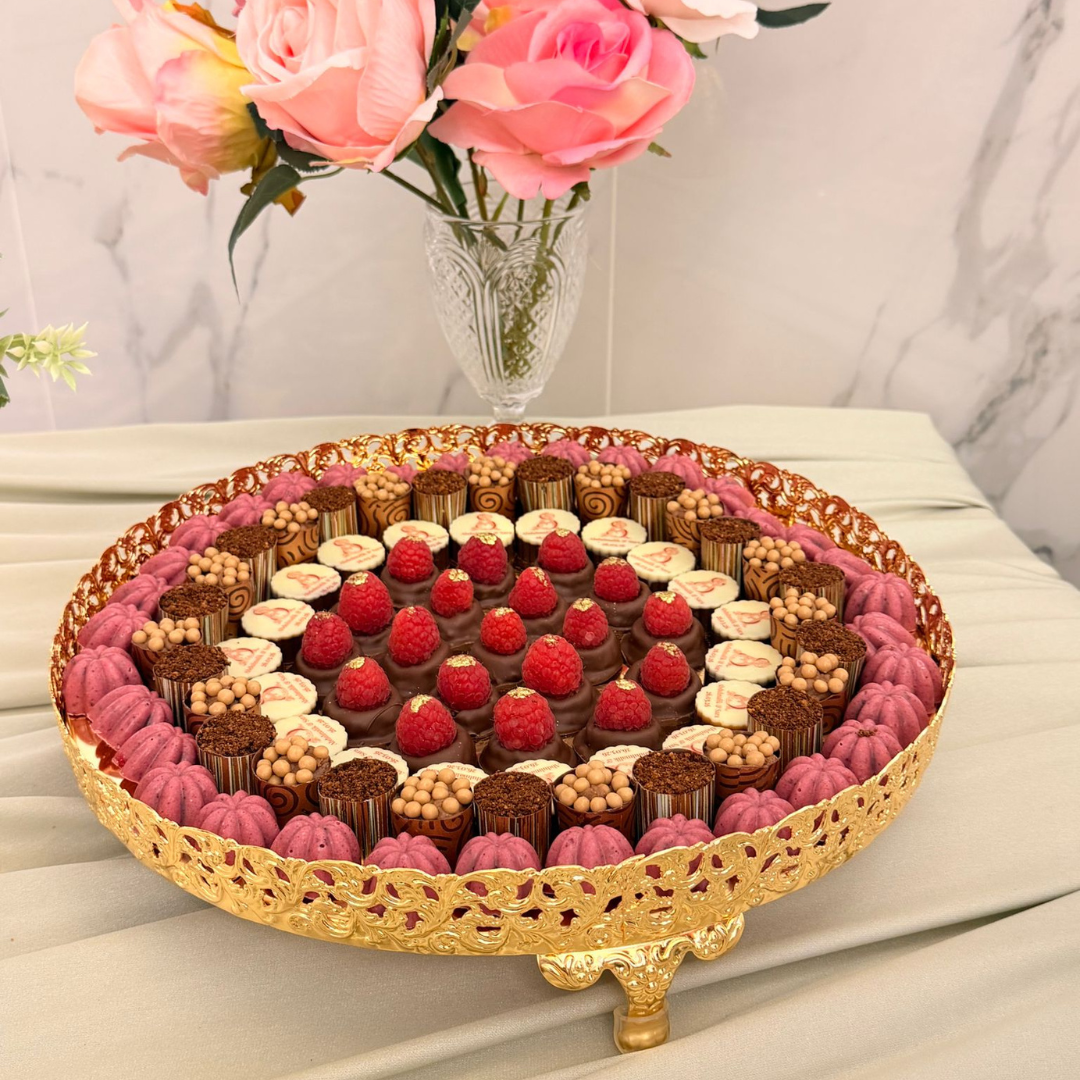 A round gold-plated decorative stand holding an assortment of luxury chocolates with fresh raspberries, personalised chocolates with the couple initials monogram, specially made Halal for arabic wedding chocolate tray in London