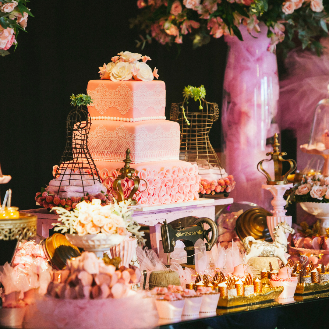 Dessert table styled in pink with a three tier lace and ruffle cake,
roses, wire dress forms, a vintage sewing machine and gold cones of
chocolates and sweets